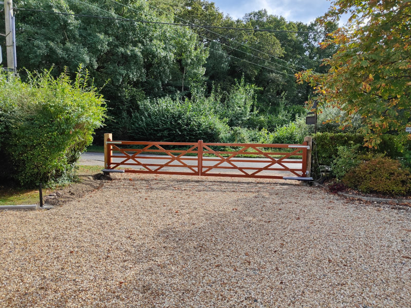 Long, wooden electric gate seperating a stoney driveway from the road